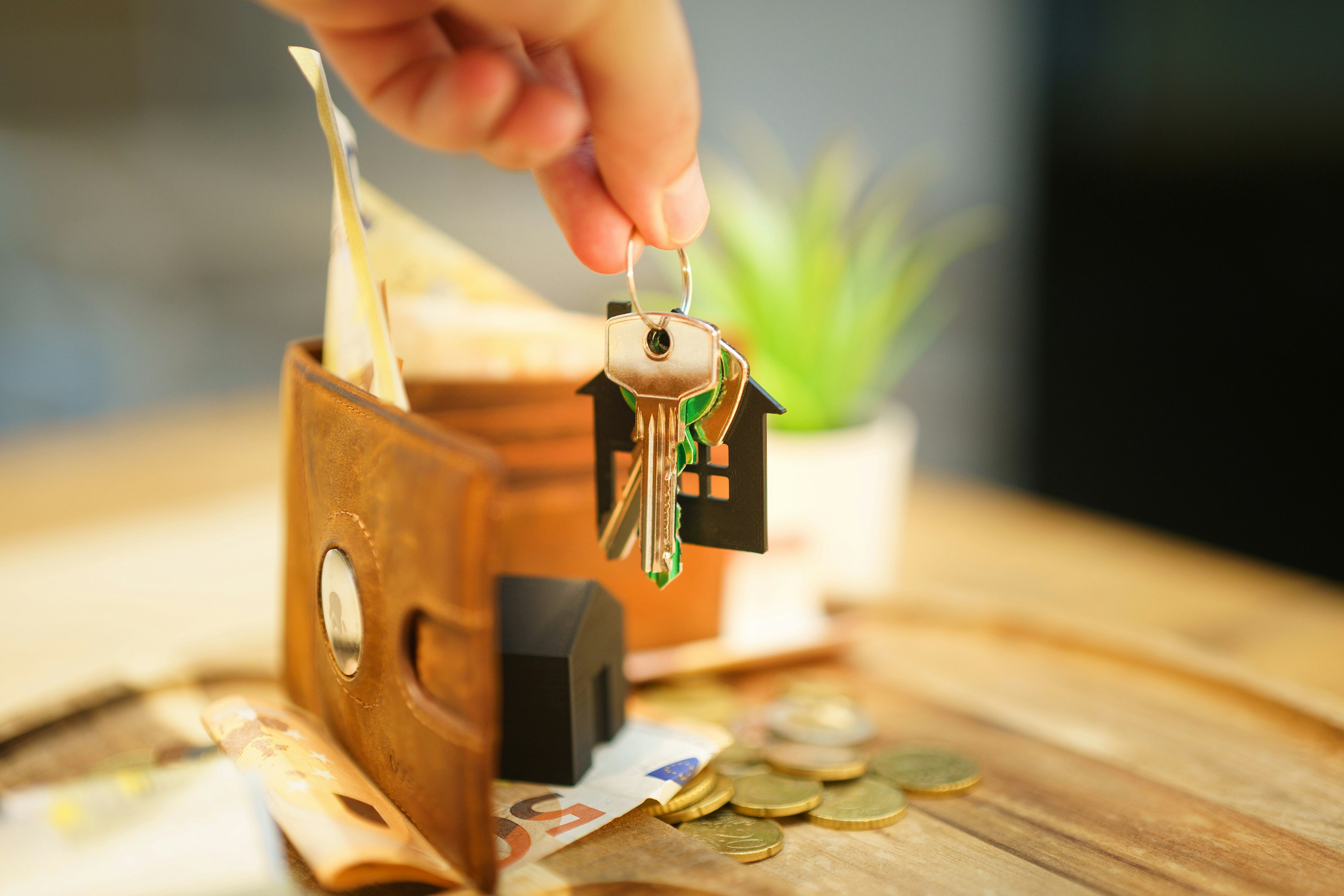 a wooden table with wallet and money a hand holds keys with a house shaped keychain indicating a contract closing