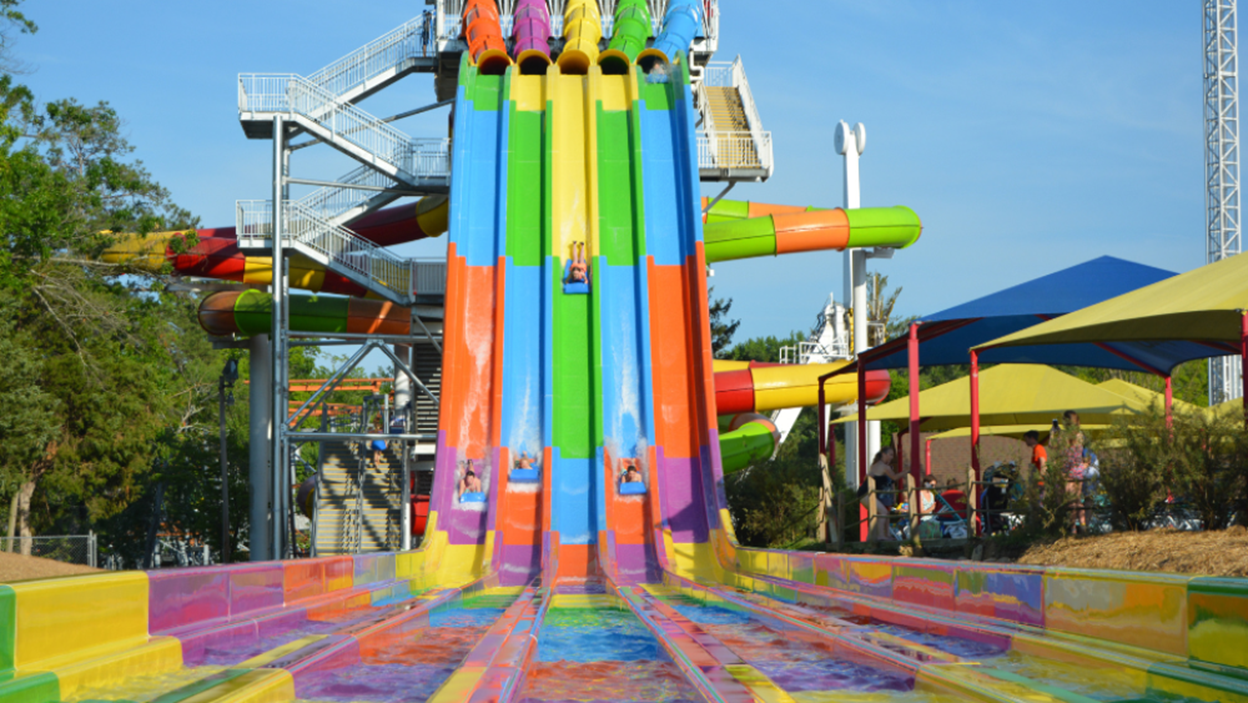 A rainbow water slide with 5 rows and people sliding down on blue boards