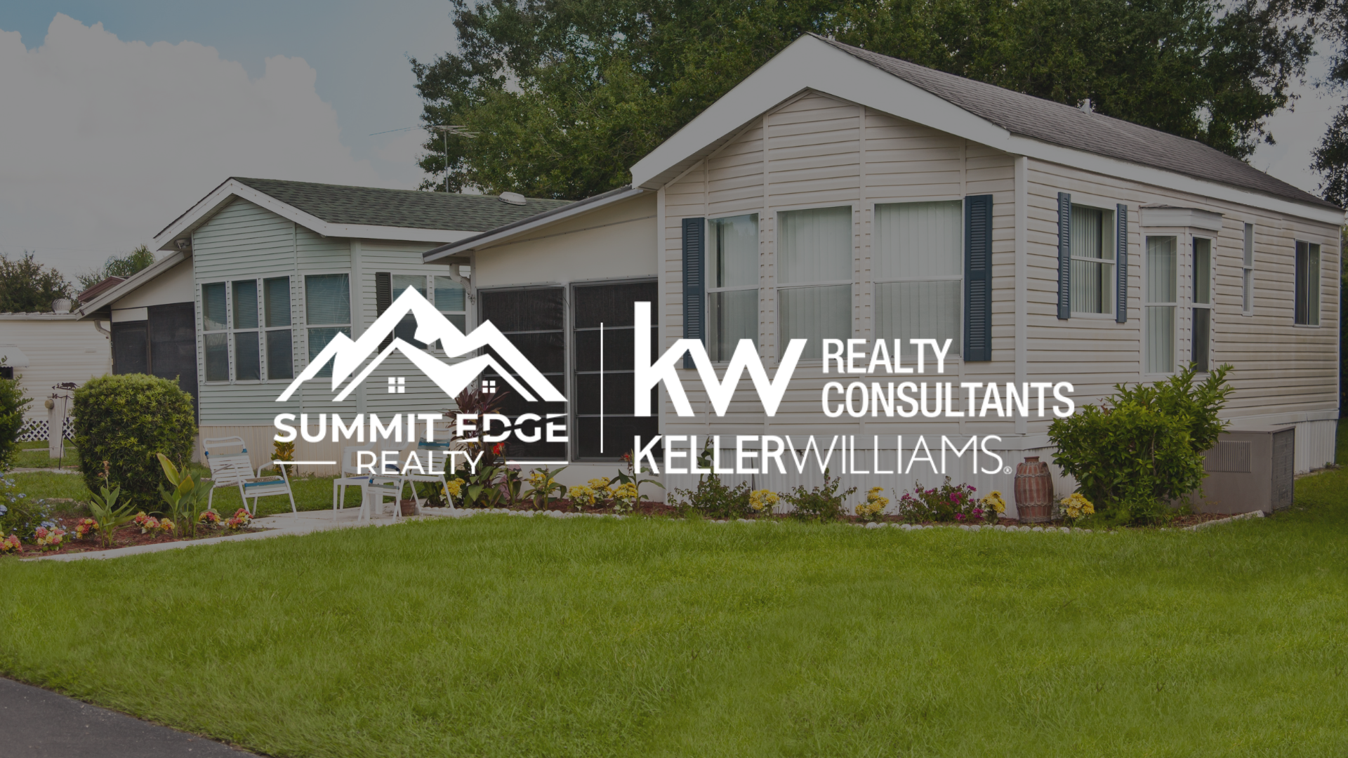 Exterior view of a Clark County, IN, manufactured home with a beige facade, small porch, and vibrant garden with flowers and shrubs, on a green lawn under a partly cloudy sky, branded with the Summit Edge Realty and KW Realty Consultants Keller Williams logo in white.