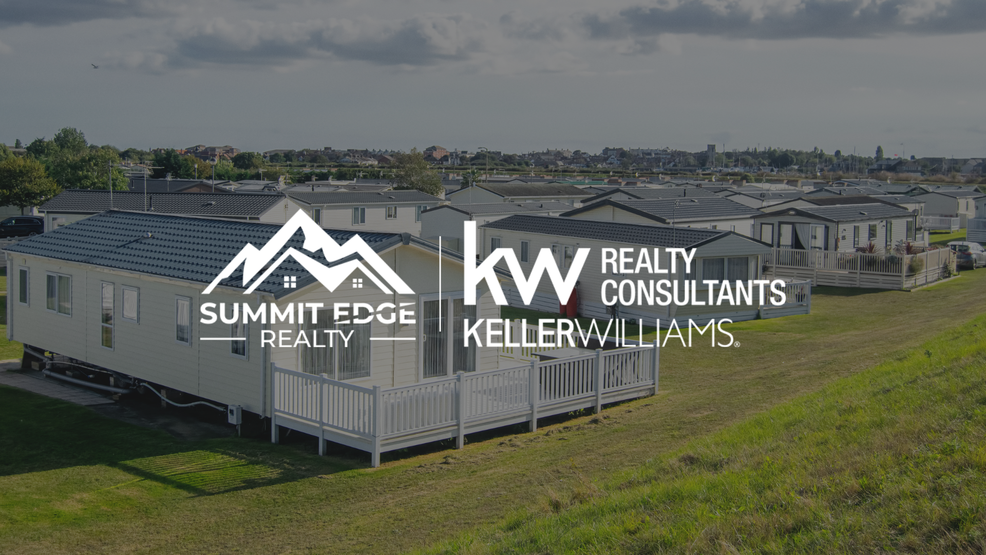 A community of manufactured homes in Clark County, IN, featuring white and gray exteriors with small porches, set on lush green lots under a cloudy sky, with trees in the background, overlaid with the Summit Edge Realty and KW Realty Consultants Keller Williams logo in white text.