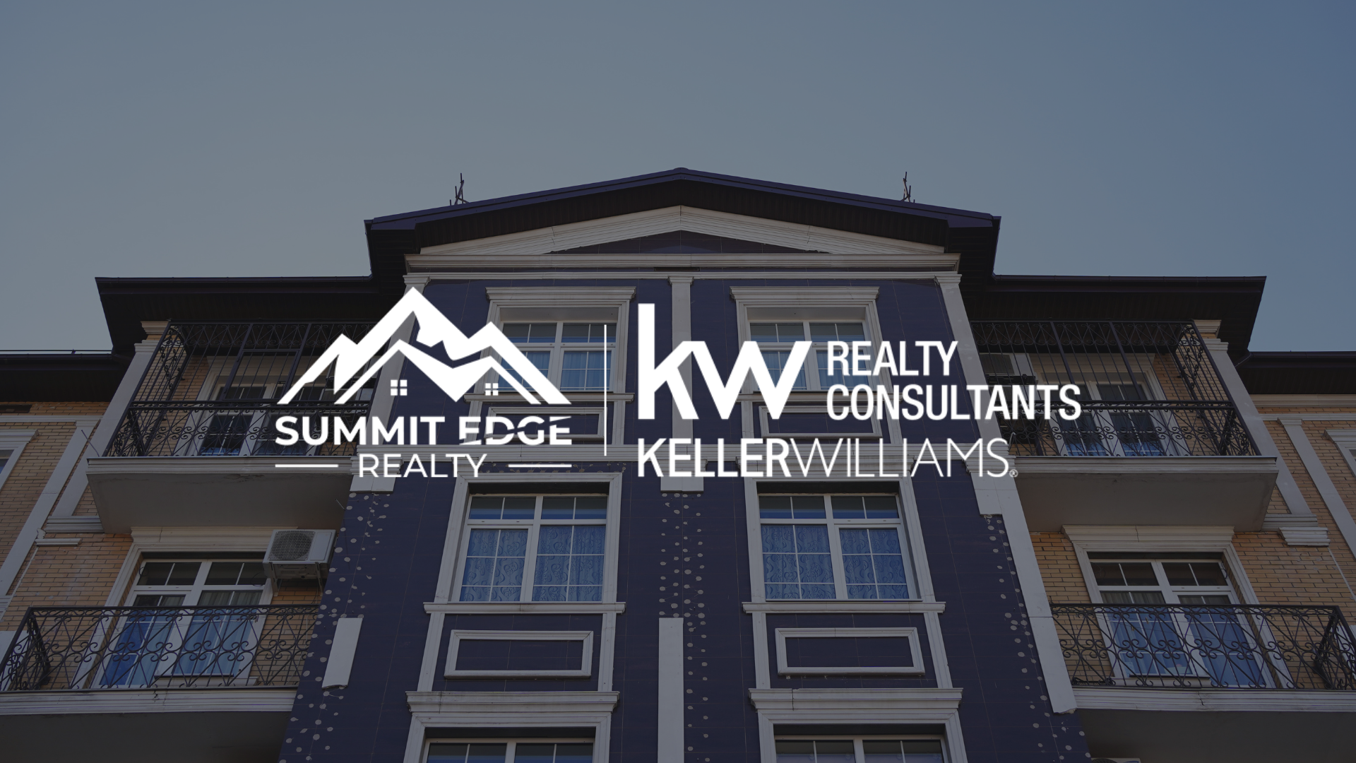 Exterior view of a modern multi-family building in Clark County, IN, with blue siding and brick accents, showcasing balconies and windows, with Summit Edge Realty and KW Realty Consultants Keller Williams branding prominently displayed.