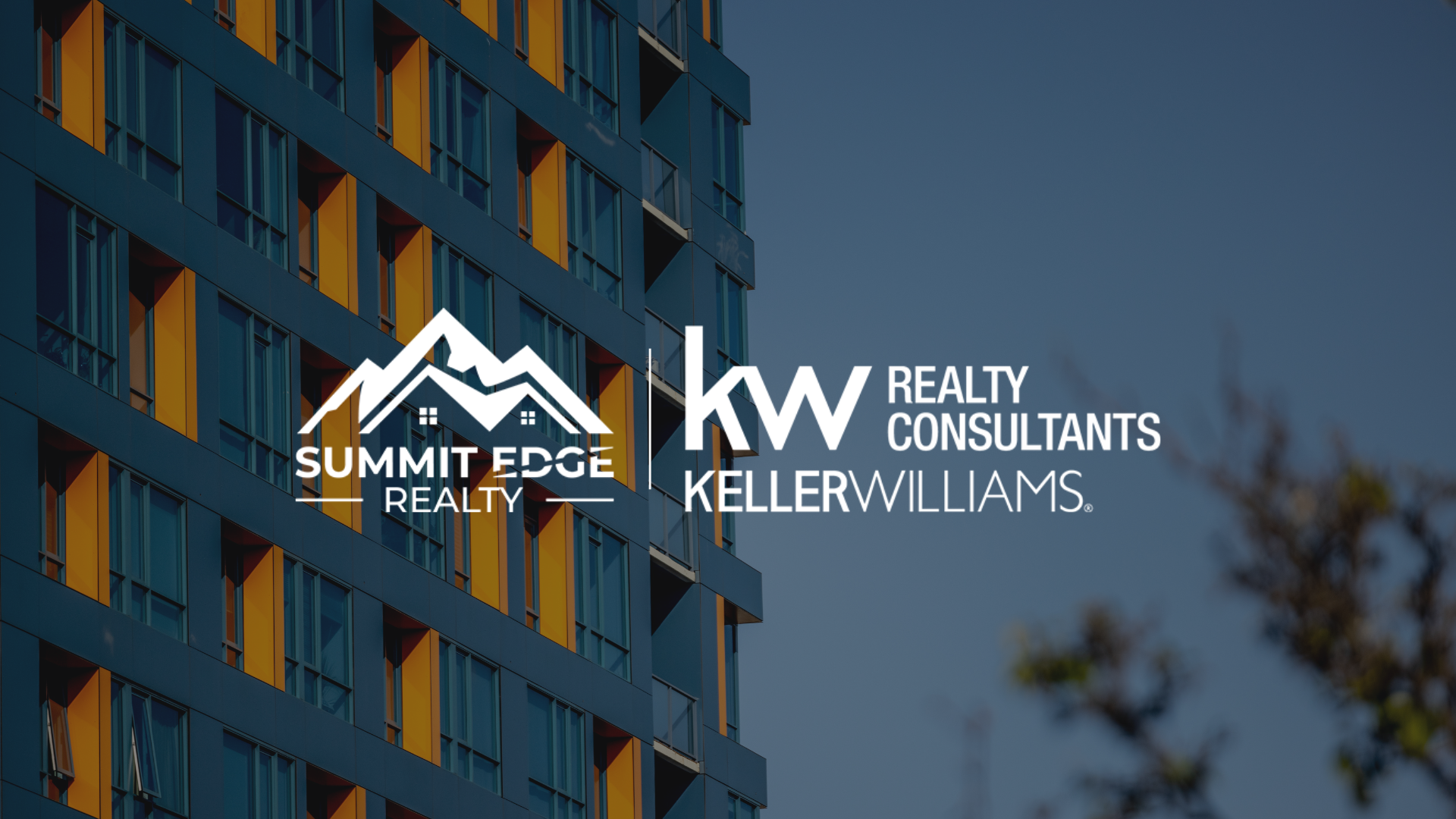 A Harrison County, IN, multifamily residence with a blue and orange exterior, featuring large windows across several floors, surrounded by trees under a clear sky, overlaid with the Summit Edge Realty and KW Realty Consultants Keller Williams logo in white.