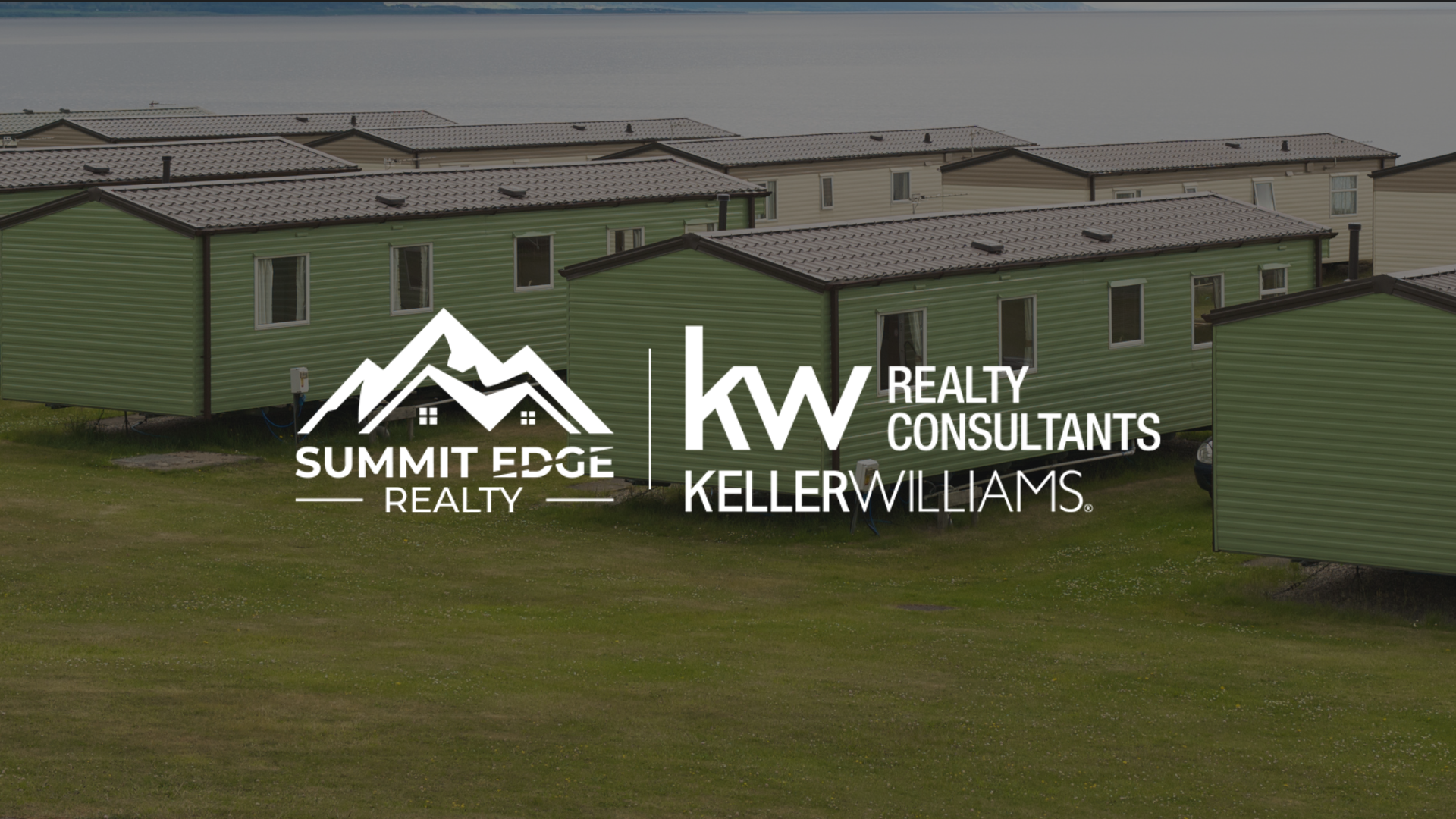 Exterior view of Louisville, KY, manufactured homes featuring green facades and pitched roofs, situated on a lush green lawn with a lake visible in the distance under a cloudy sky, branded with the Summit Edge Realty and KW Realty Consultants Keller Williams logo in white.