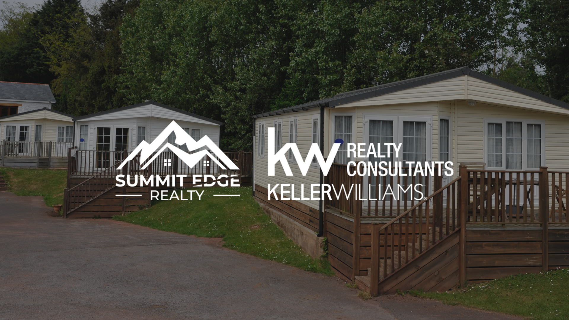 A modern manufactured home in Floyd County, IN, with a white exterior, a spacious front deck with potted plants, and a gravel driveway, surrounded by a grassy lawn and trees under a sunny June sky, overlaid with the Summit Edge Realty and KW Realty Consultants Keller Williams logo in white text.