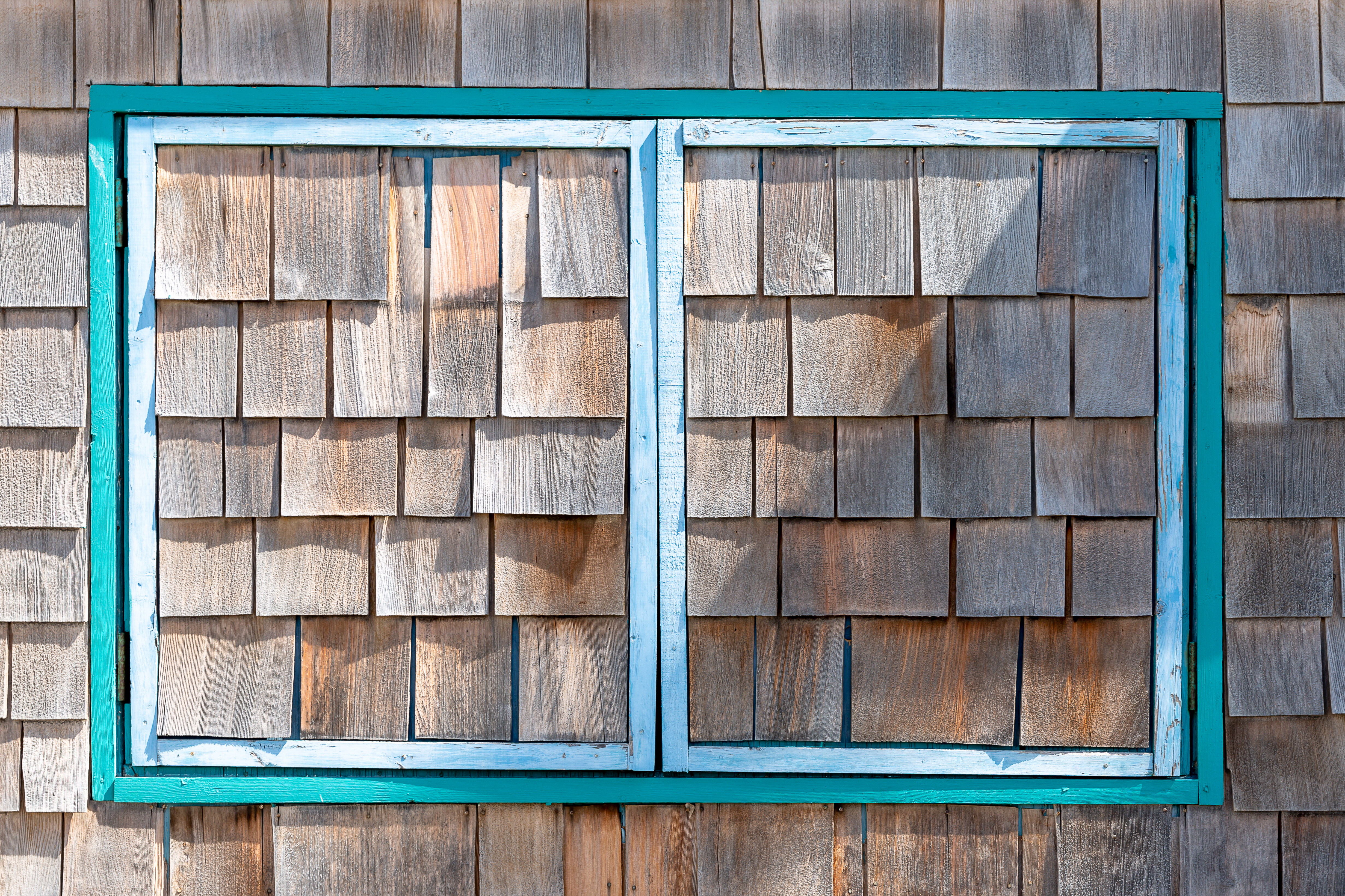Weathered cedar shingle siding with teal-framed window on a Pacific Beach home