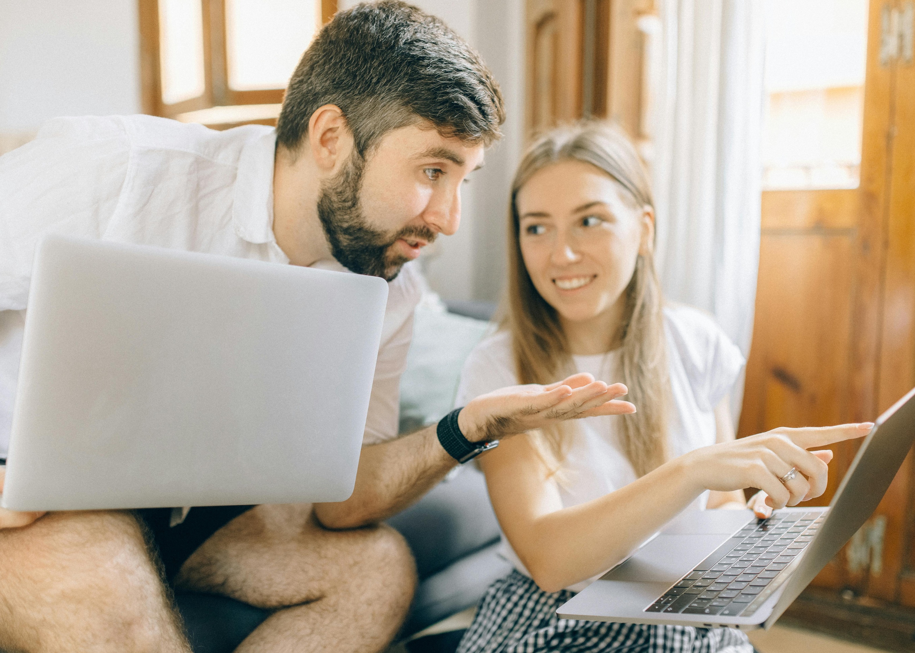 A young couple sitting next to each other, looking at a laptop, slightly concerned.