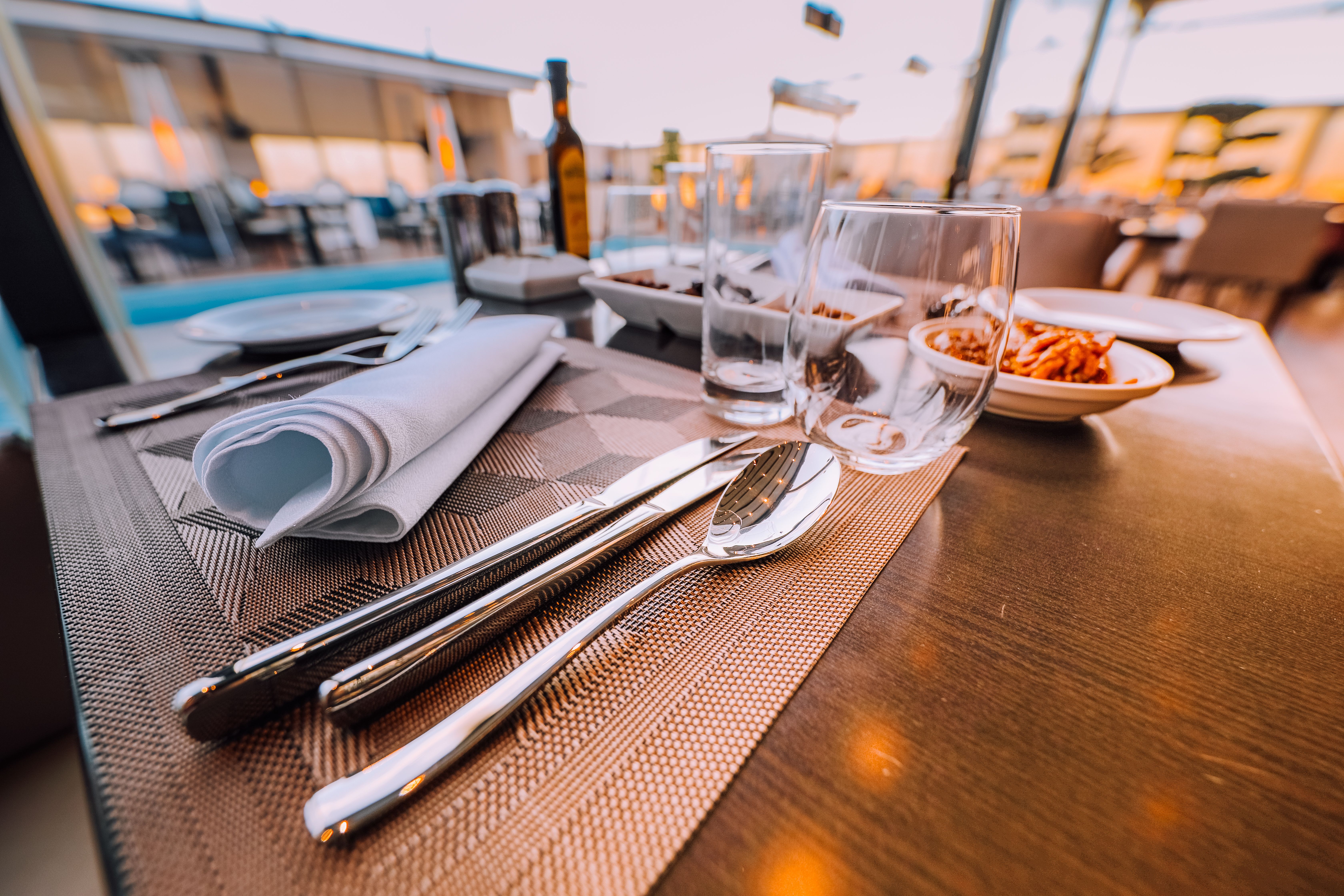 Restaurant table set with silverware, white napkins, glasses, and plates of food overlooking an outdoor dining area.