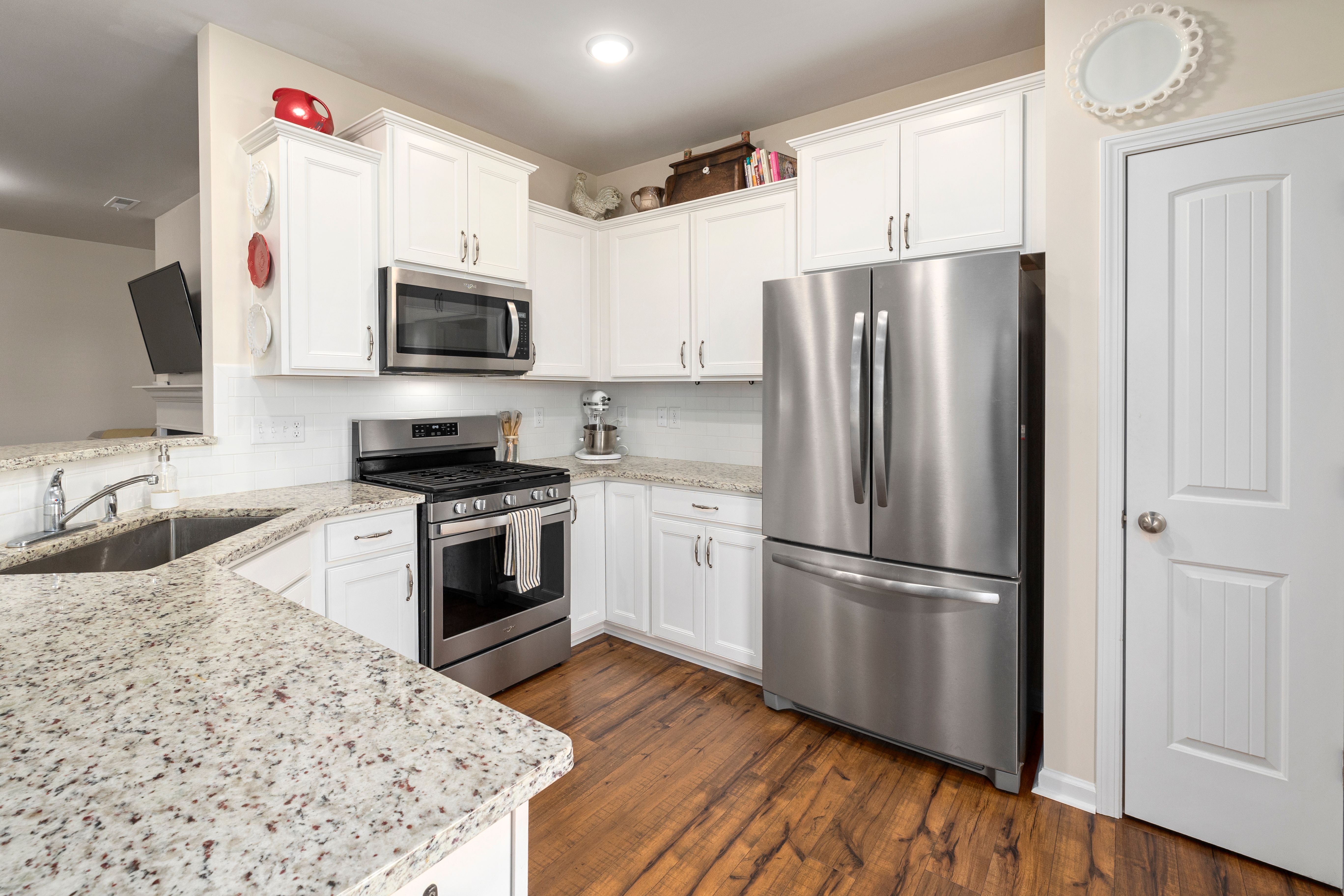 Bright modern kitchen with white cabinets, granite countertops, stainless steel appliances, and hardwood flooring.