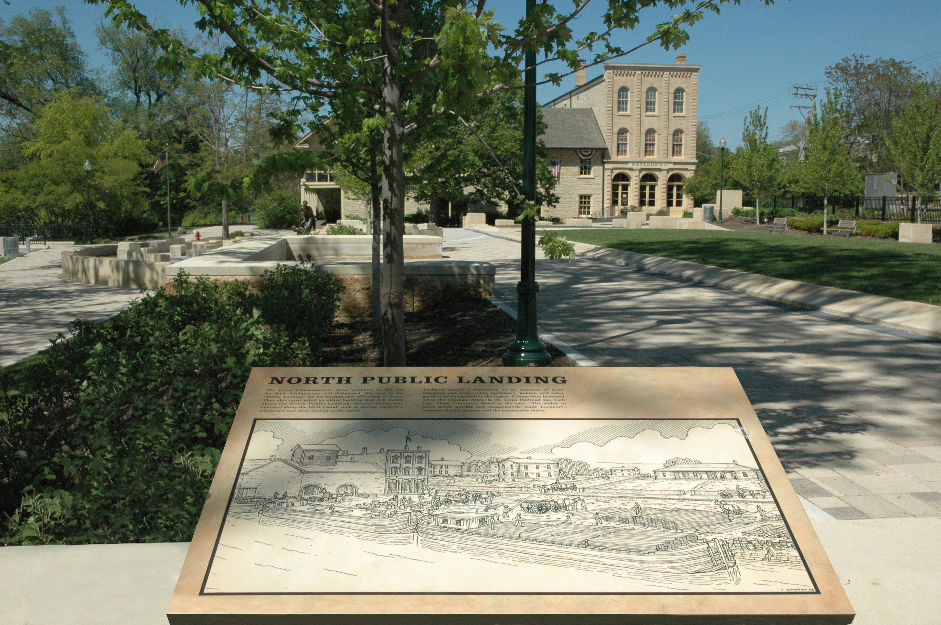 North Public Landing historical marker in downtown Lockport, Illinois, featuring the I&M Canal heritage site, landscaped park area, walking paths, and historic architecture.
