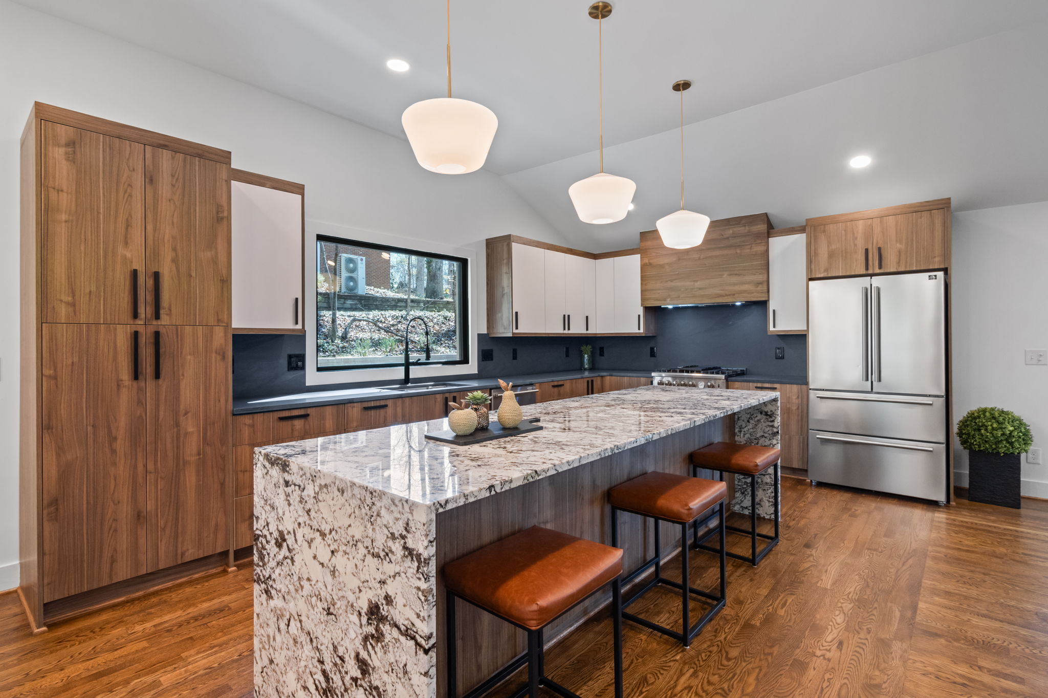 Modern kitchen with large marble island, wood and white cabinetry, stainless steel appliances, and pendant lighting.