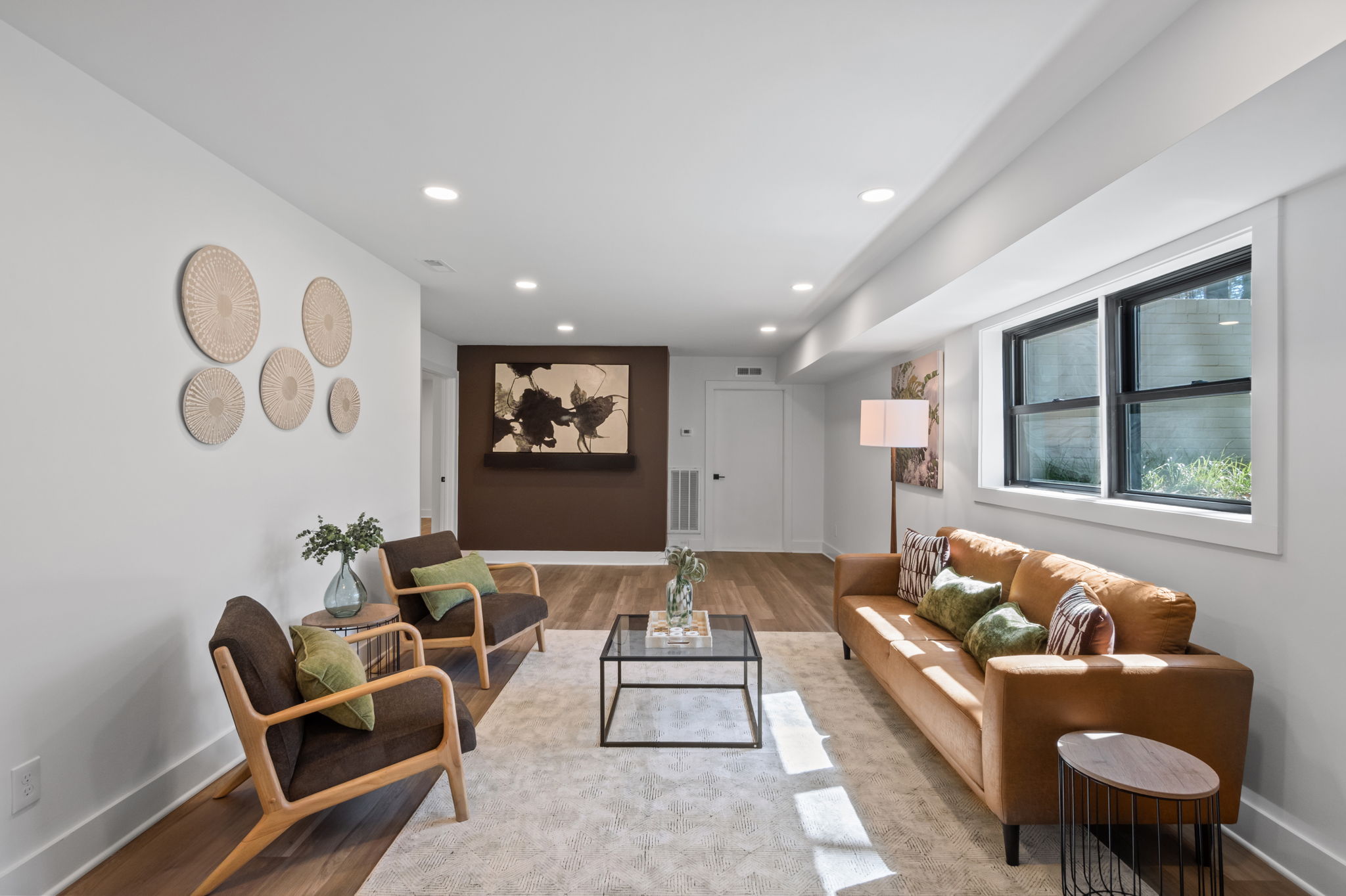 Finished lower-level living room with seating area, wood accent wall, and windows bringing in natural light