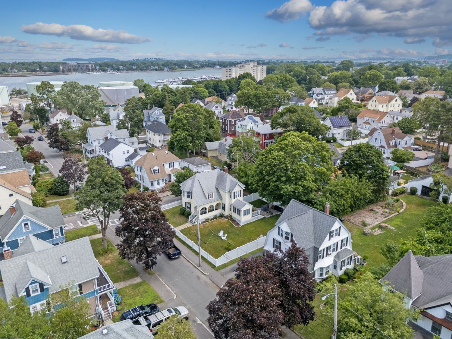 Aerial view of a tree-lined Quincy, MA neighborhood with single-family homes and the harbor and marina in the distance